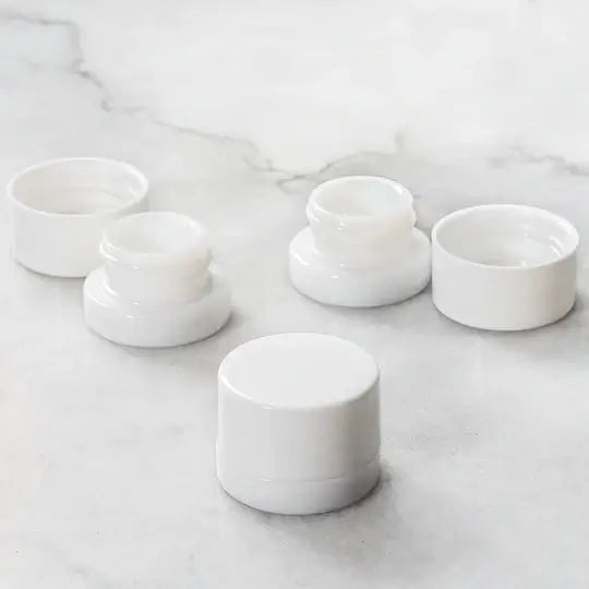5ml round white glass concentrate jars arranged on a marble surface, showcasing their compact design.