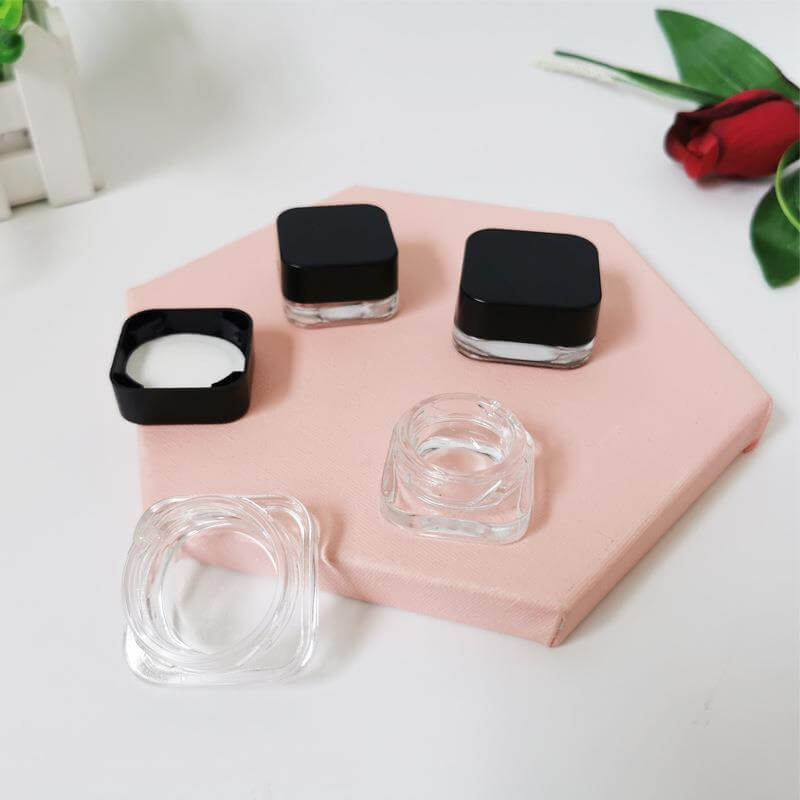 5 ML square clear glass jars with black lids on a pink surface, perfect for cosmetics and extracts.