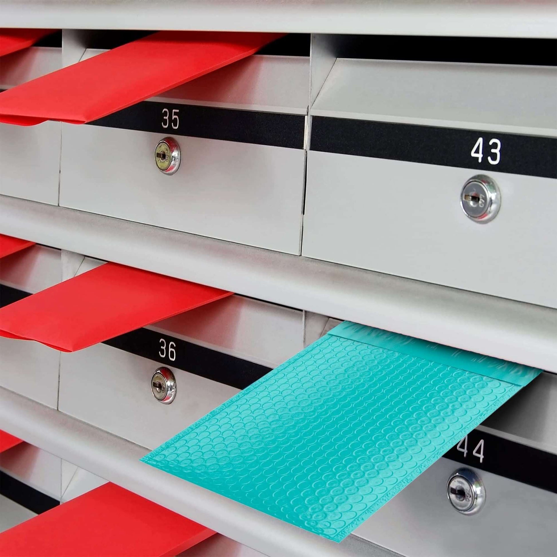 Teal poly bubble mailer peeking out from a mail slot among red envelopes in a row of mailboxes.