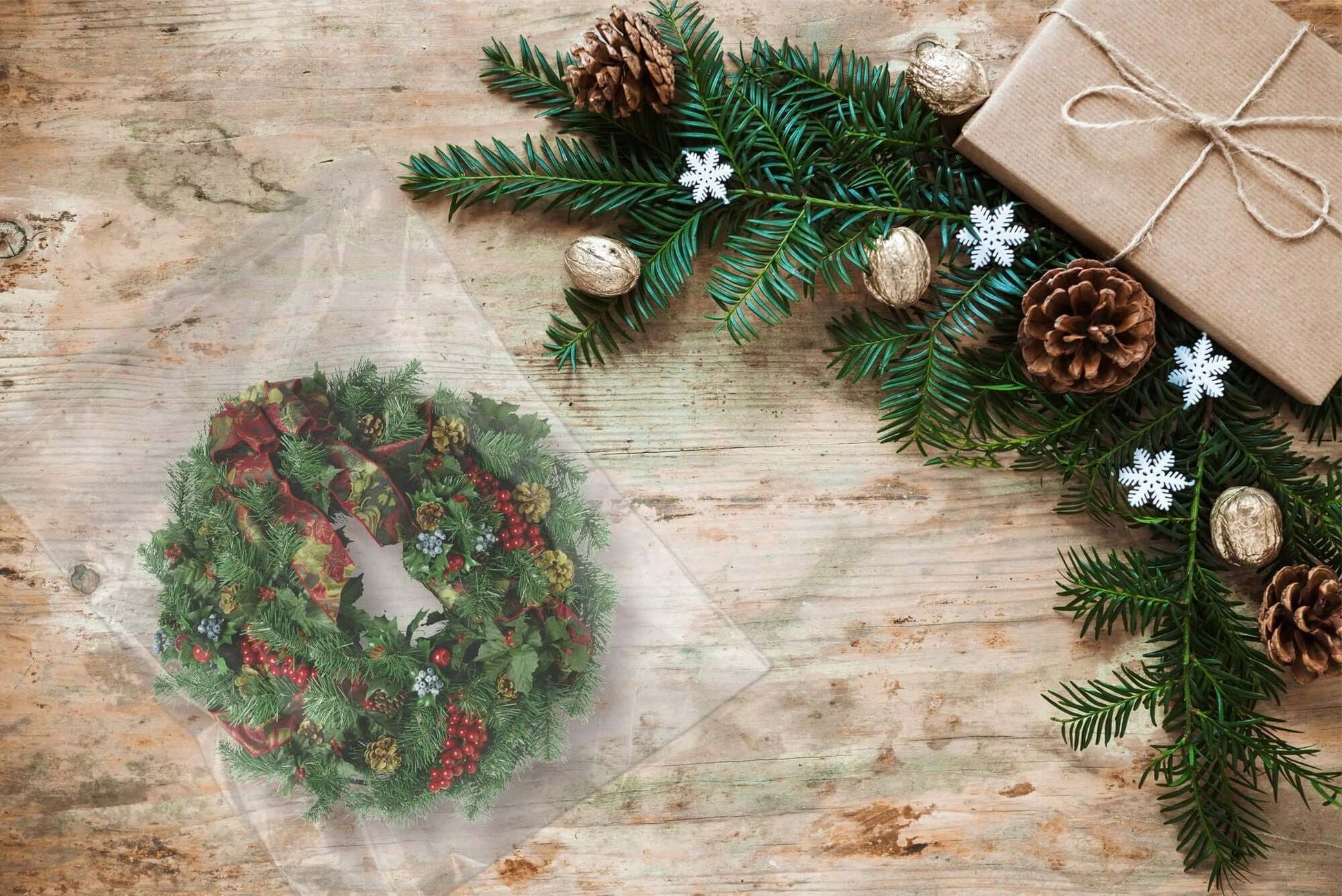 Festive holiday wreath on rustic wood with pinecones, gift box, and evergreen branches.