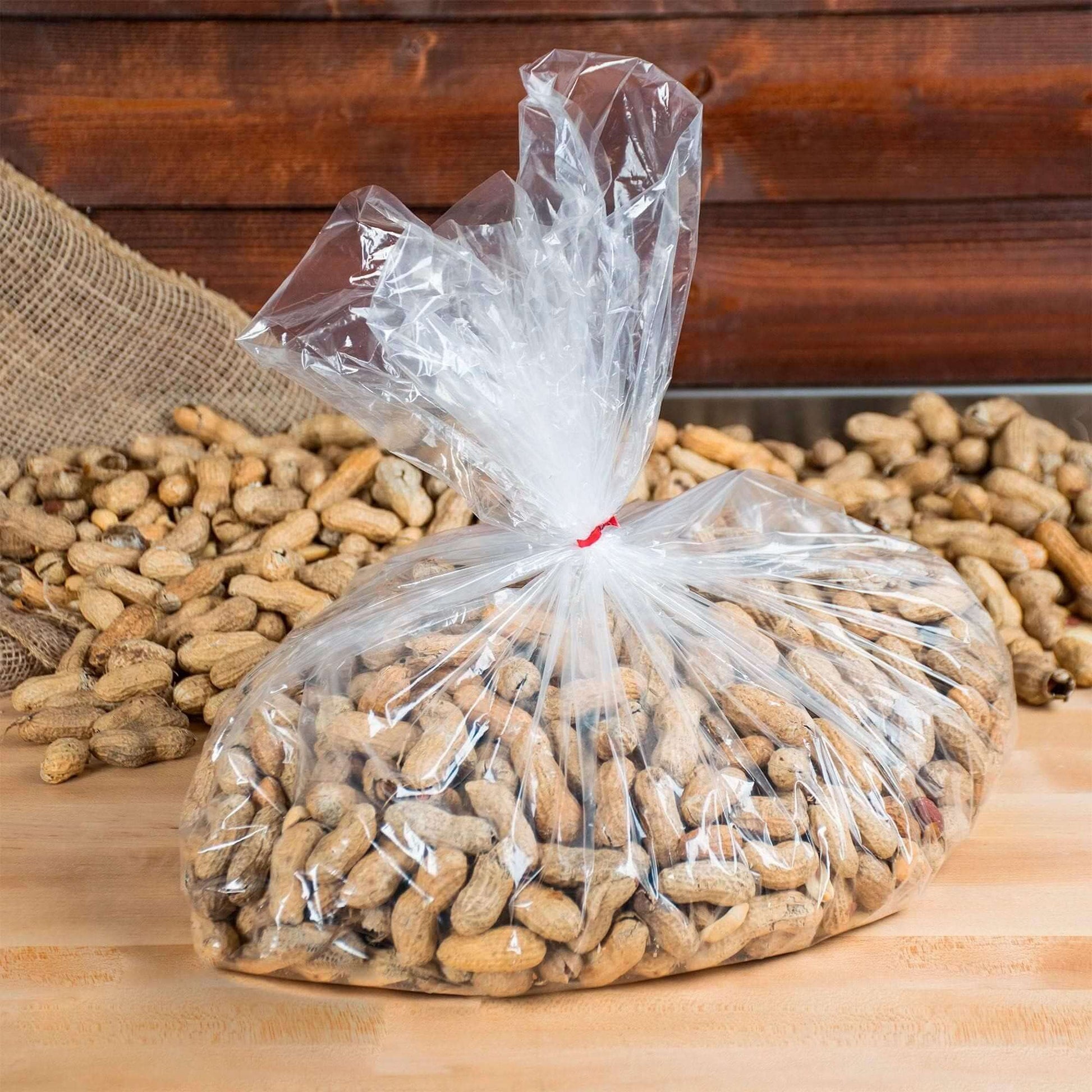 Clear gusseted poly bag filled with raw peanuts on a wooden surface.