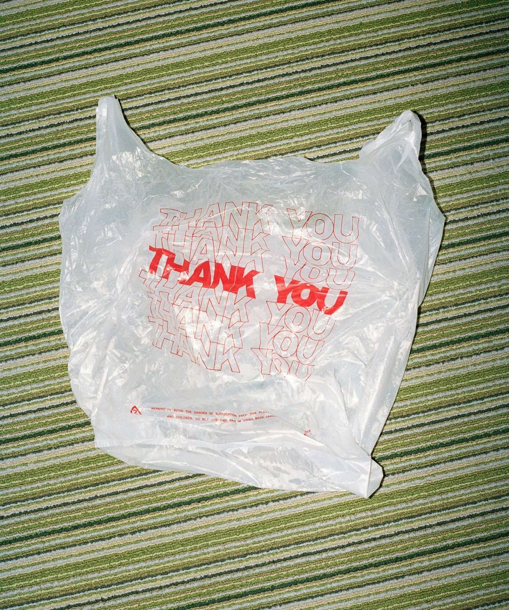 Pack of white plastic Thank You bags with red lettering on a green striped surface.